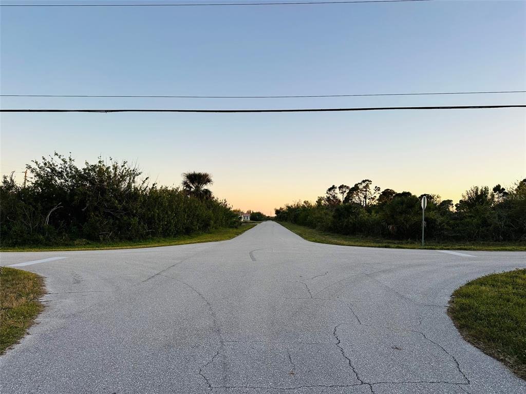 An asphalt road stretches into the distance at a rural intersection surrounded by vegetation — 12204 ZITTLE AVENUE, PORT CHARLOTTE, FL