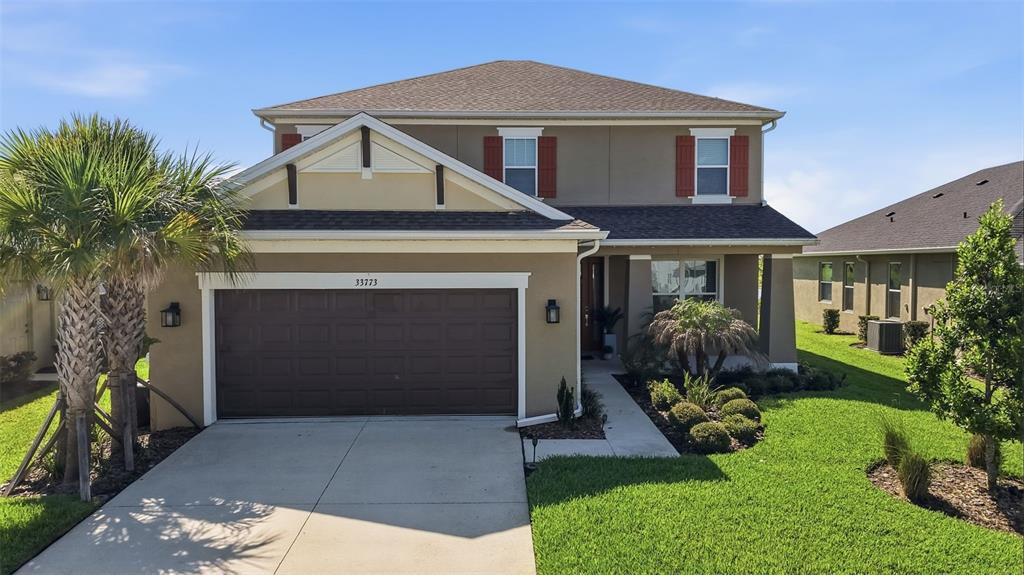 A two-story suburban house with a tan stucco exterior, brown roof, and a two-car garage — 33773 ASTORIA CIRCLE, WESLEY CHAPEL, FL