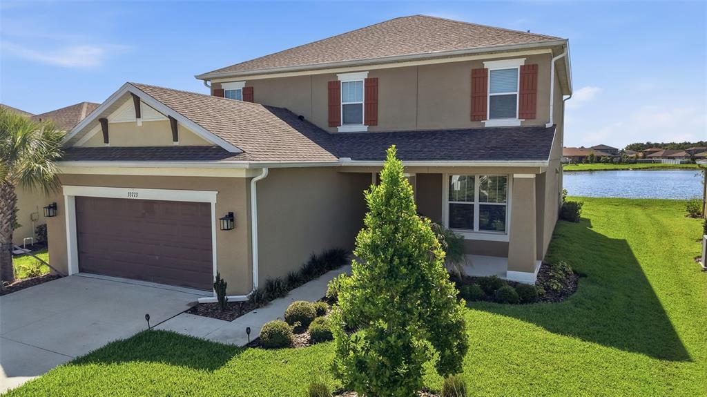 A two-story suburban house with a tan stucco exterior, brown roof, and attached garage — 33773 ASTORIA CIRCLE, WESLEY CHAPEL, FL