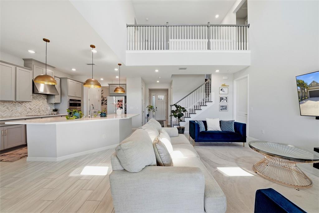 An open-concept living room and kitchen featuring light wood floors, a loft, and stairs — 33773 ASTORIA CIRCLE, WESLEY CHAPEL, FL