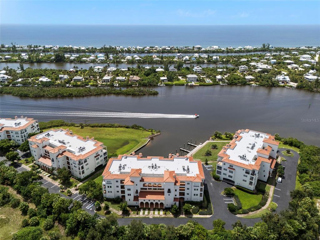 An aerial view shows three multi-story apartment buildings situated along a waterfront with a boat — 11120 HACIENDA DEL MAR BOULEVARD UNIT F-205, PLACIDA, FL