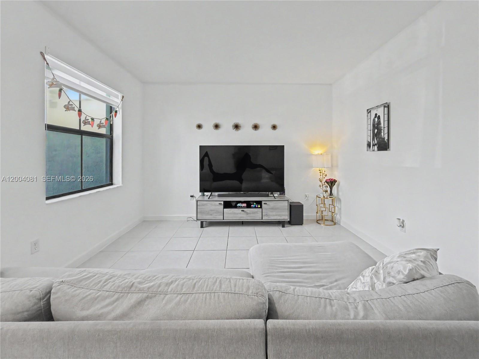 A living room features white walls, tile flooring, a grey sofa, and a television console — 14800 SW 183rd Ter, Miami FL 33187, MIAMI, FL