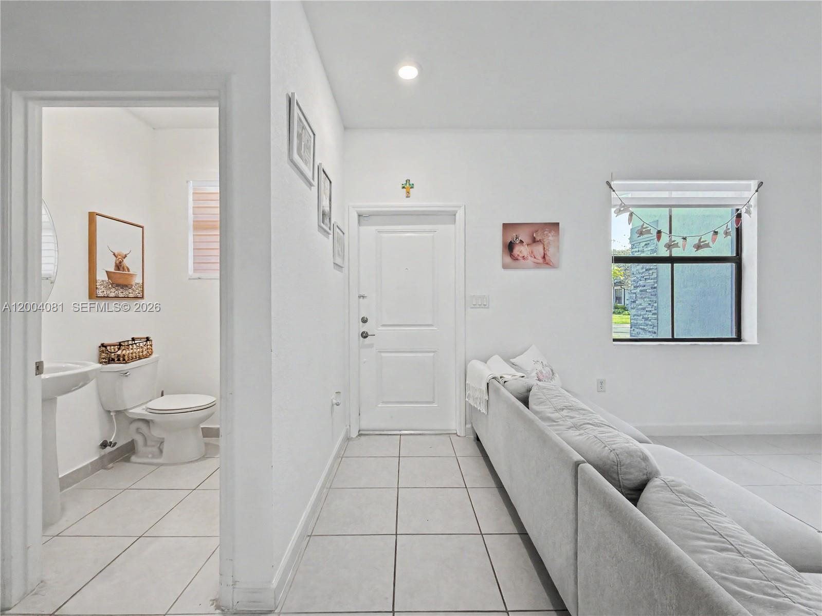 A living room with white tile floors, a grey sofa, and an adjacent half bathroom — 14800 SW 183rd Ter, Miami FL 33187, MIAMI, FL