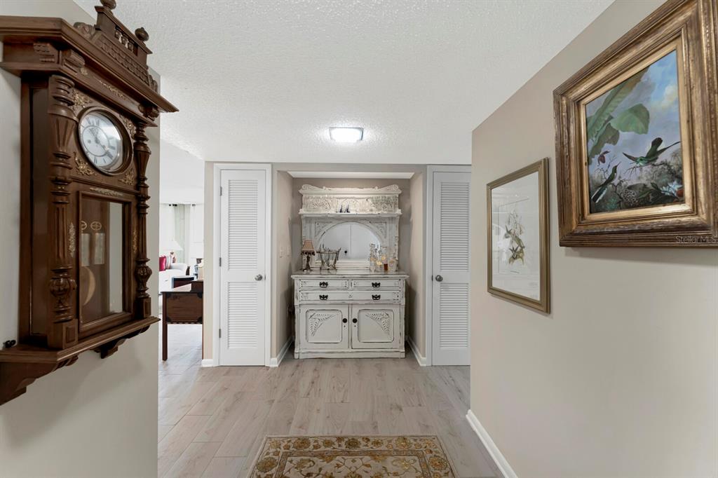A hallway features a wall-mounted clock, a white hutch, and framed art on light walls — 1430 GULF BOULEVARD UNIT 108, CLEARWATER, FL