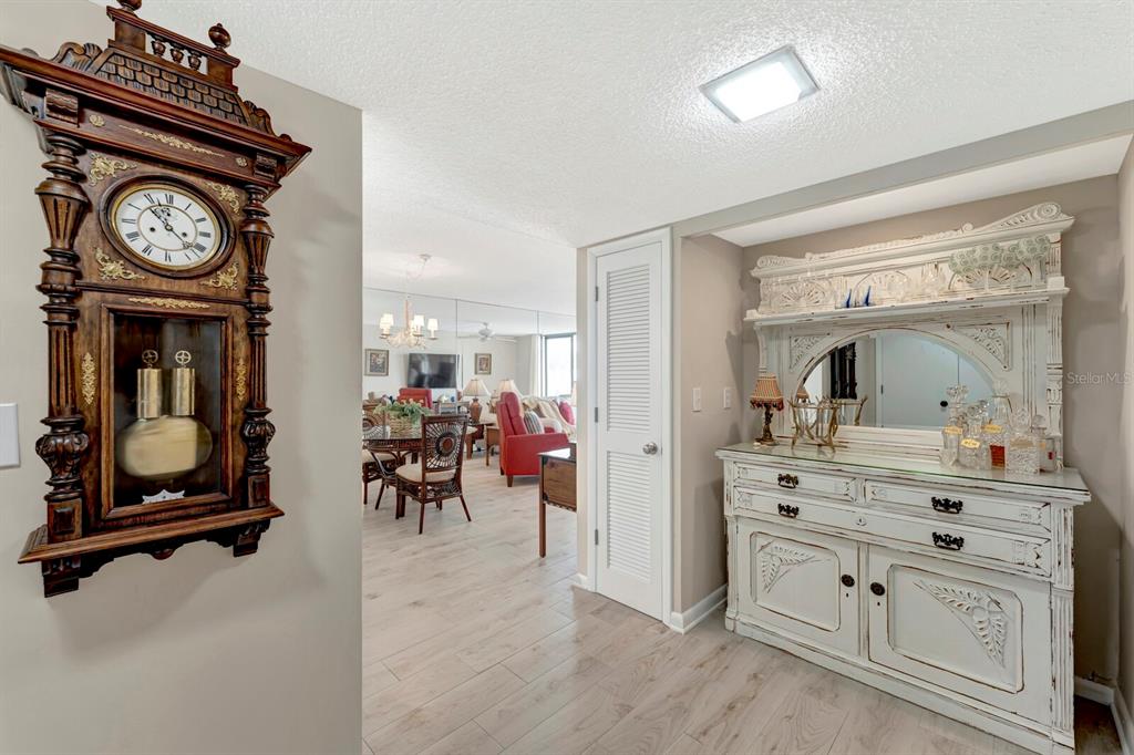 A hallway features a wooden wall clock, a white sideboard with a mirror, and tiled flooring — 1430 GULF BOULEVARD UNIT 108, CLEARWATER, FL