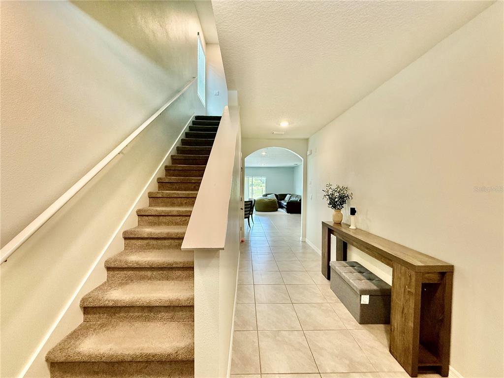 A carpeted staircase leads upstairs next to a tiled hallway with a console table — 30807 PENNY SURF LOOP, WESLEY CHAPEL, FL