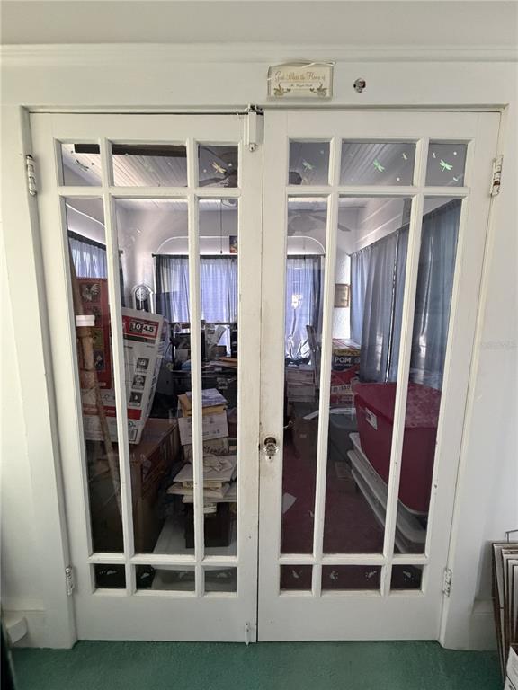 A pair of white French doors with glass panes opens into a cluttered sunroom — 600 5TH AVENUE, DAYTONA BEACH, FL