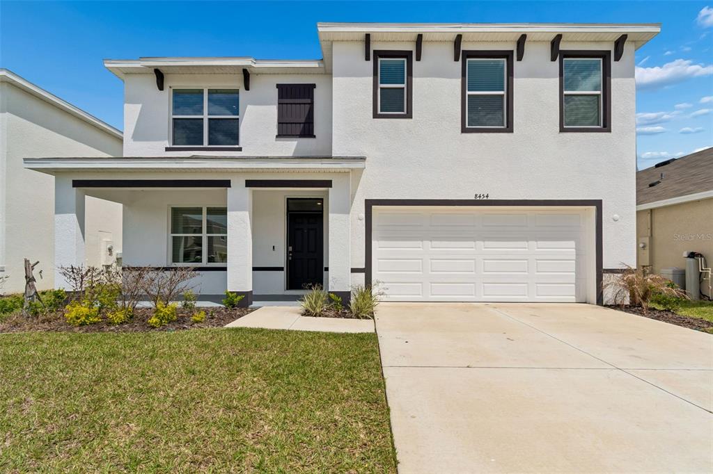 A two-story white stucco house features a front porch, a garage, and dark trim — 8454 ENDER HILLS DRIVE, WESLEY CHAPEL, FL