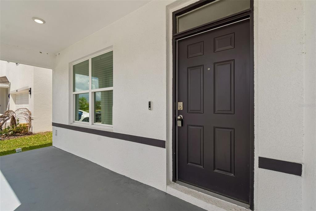 A covered porch with a dark front door, a window, and white stucco walls — 8454 ENDER HILLS DRIVE, WESLEY CHAPEL, FL