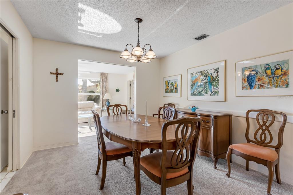A dining room features a wooden table, chairs with orange cushions, and parrot-themed wall art — 535 S PENINSULA AVENUE, NEW SMYRNA BEACH, FL