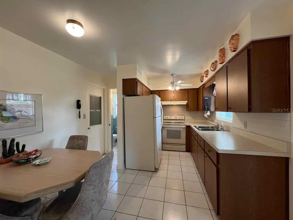 A kitchen with wood cabinets, white appliances, and tile flooring opens to a dining area — 535 S PENINSULA AVENUE, NEW SMYRNA BEACH, FL