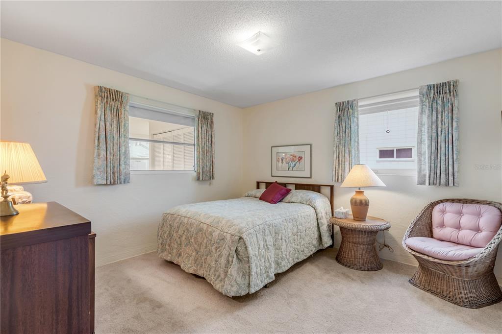 A bedroom features a bed, a wicker chair, two windows with curtains, and carpeted flooring — 535 S PENINSULA AVENUE, NEW SMYRNA BEACH, FL