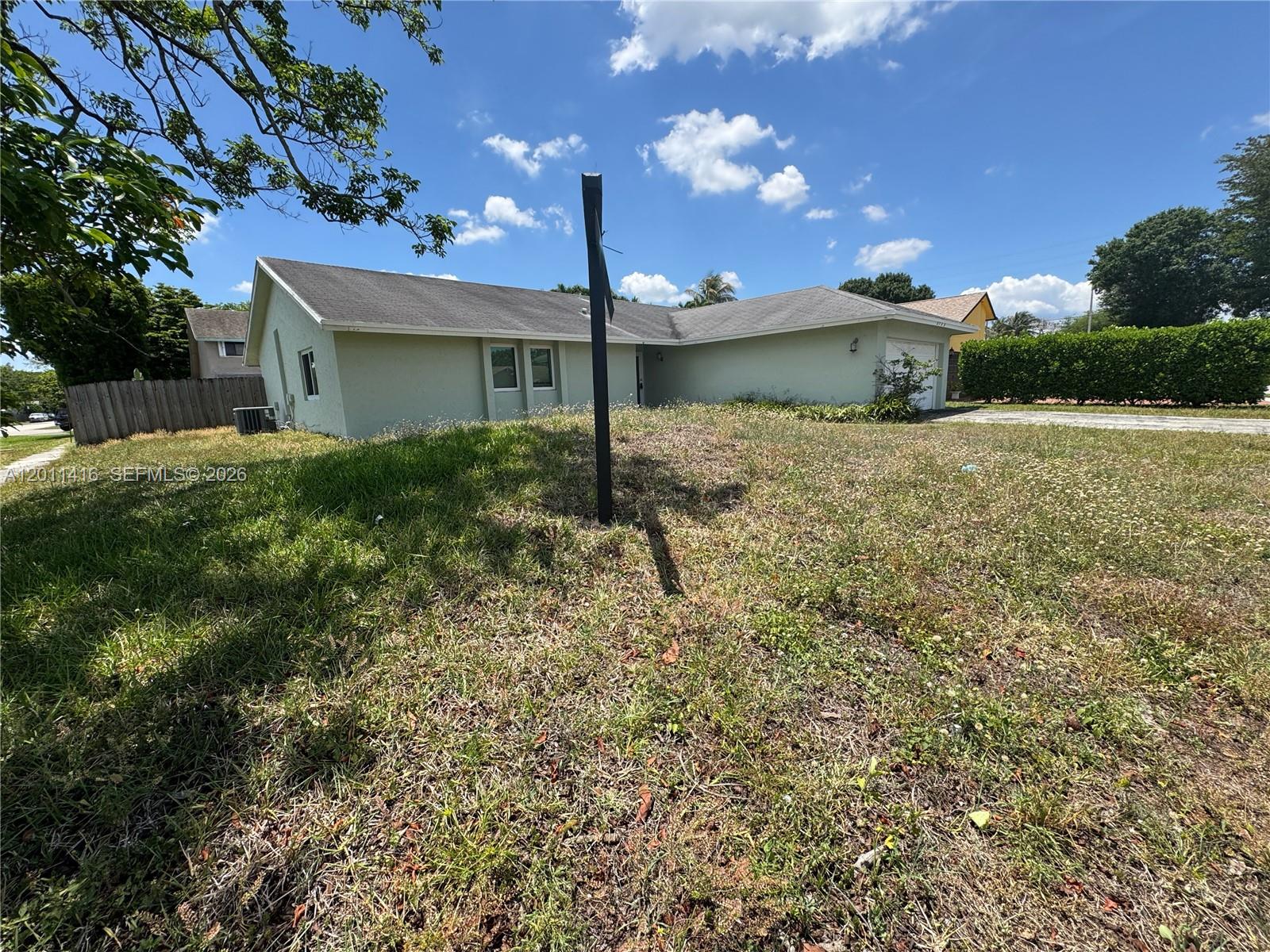 A single-story house with a light green exterior and a large, overgrown front yard — 8700 NW 46th Ct, Lauderhill FL 33351, LAUDERHILL, FL