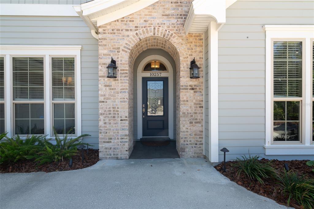 The front exterior features a dark blue door with a glass insert under a brick archway — 10257 SW 37TH PLACE, GAINESVILLE, FL