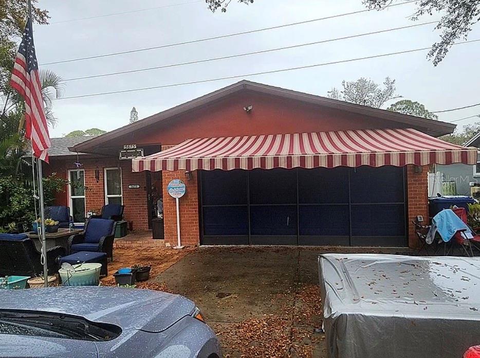 A brick house exterior features a striped retractable awning over a dark garage door — 5673 97TH WAY N, ST PETERSBURG, FL