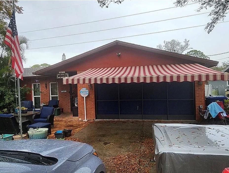 A brick house features a striped retractable awning over a dark garage screen door — 5673 97TH WAY N, ST PETERSBURG, FL