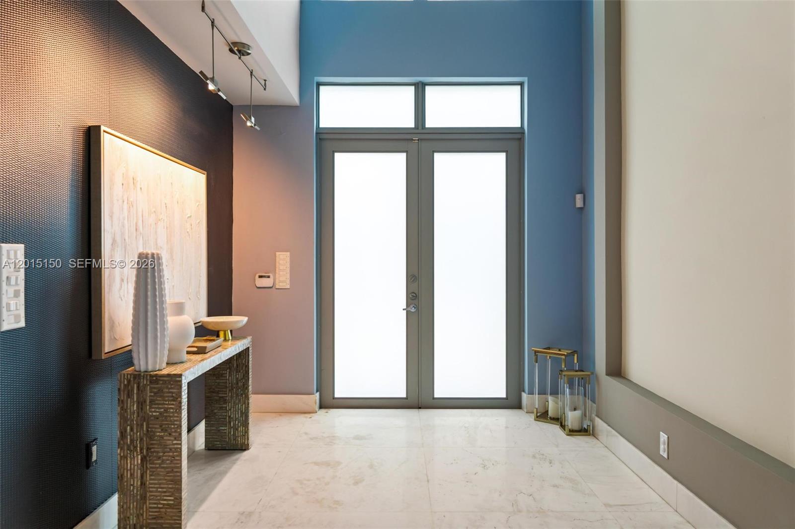 A modern entryway features a console table, double glass doors, and blue accent walls — 3917 S Le Jeune Rd, Miami FL 33146, MIAMI, FL