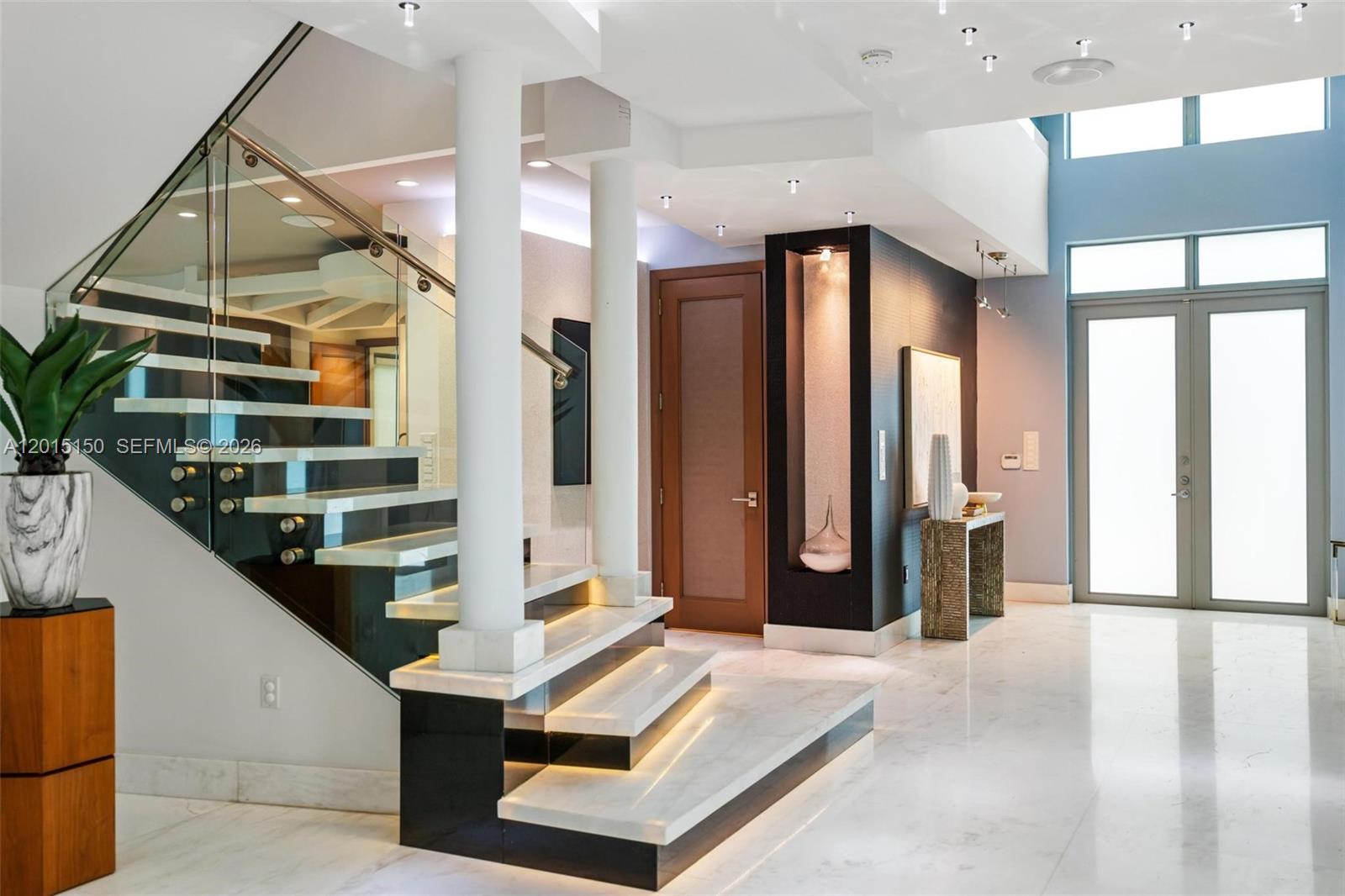 A modern foyer features a floating staircase with glass railings, marble floors, and recessed lighting — 3917 S Le Jeune Rd, Miami FL 33146, MIAMI, FL