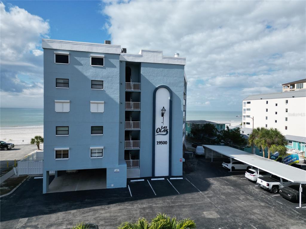An exterior view of a blue multi-story apartment building with a parking lot — 19500 GULF BOULEVARD UNIT 102, INDIAN SHORES, FL