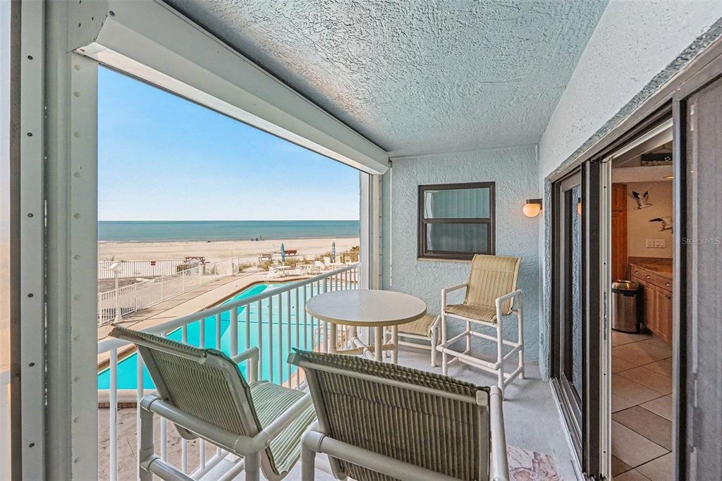 A balcony with patio furniture overlooks a swimming pool and the ocean beach — 19500 GULF BOULEVARD UNIT 102, INDIAN SHORES, FL