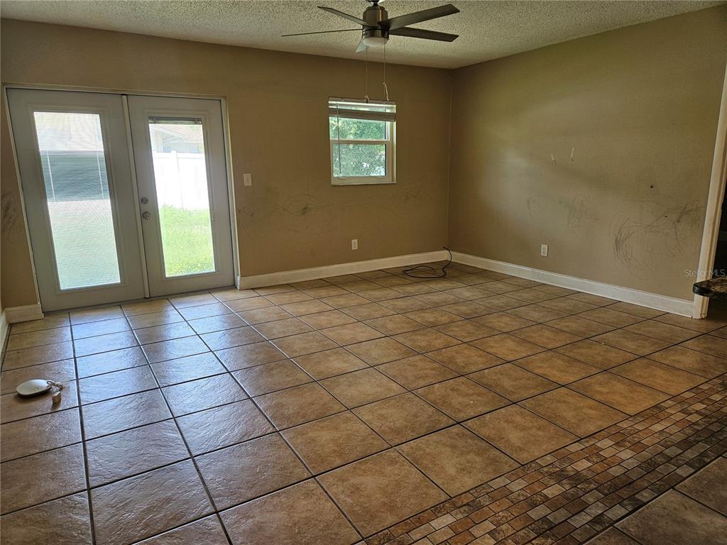 An empty room features tan tile flooring, a ceiling fan, and glass double doors — 6092 BURCH STREET N, ST PETERSBURG, FL