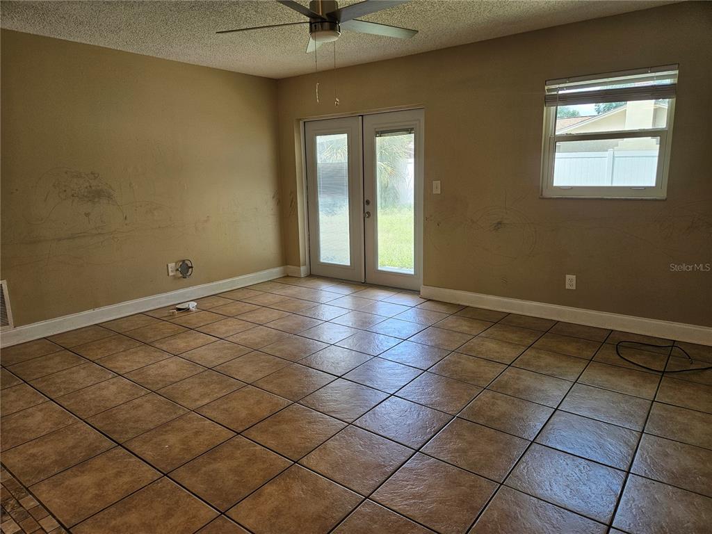 An empty room features tan walls with scuff marks, tile flooring, a ceiling fan, and doors — 6092 BURCH STREET N, ST PETERSBURG, FL