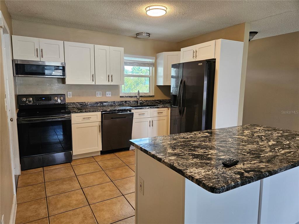 A kitchen features white cabinets, granite countertops, a kitchen island, and black appliances — 6092 BURCH STREET N, ST PETERSBURG, FL