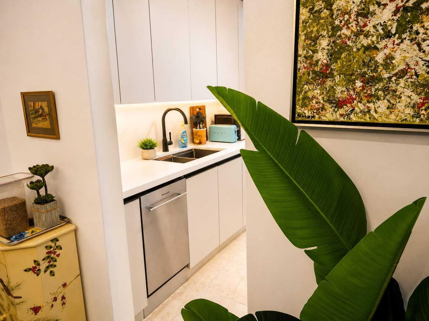 A modern kitchen features white cabinetry, a stainless steel dishwasher, and a light-colored countertop — 16900 NE 14th Avenue # 115, Miami FL 33162, MIAMI, FL