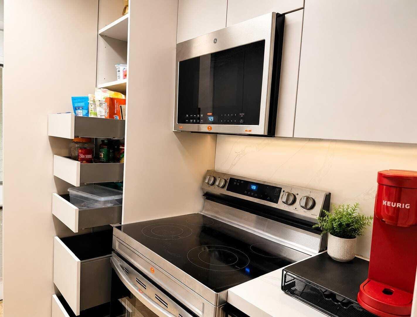 A modern kitchen features a stainless steel microwave, electric range, and a pull-out pantry cabinet — 16900 NE 14th Avenue # 115, Miami FL 33162, MIAMI, FL