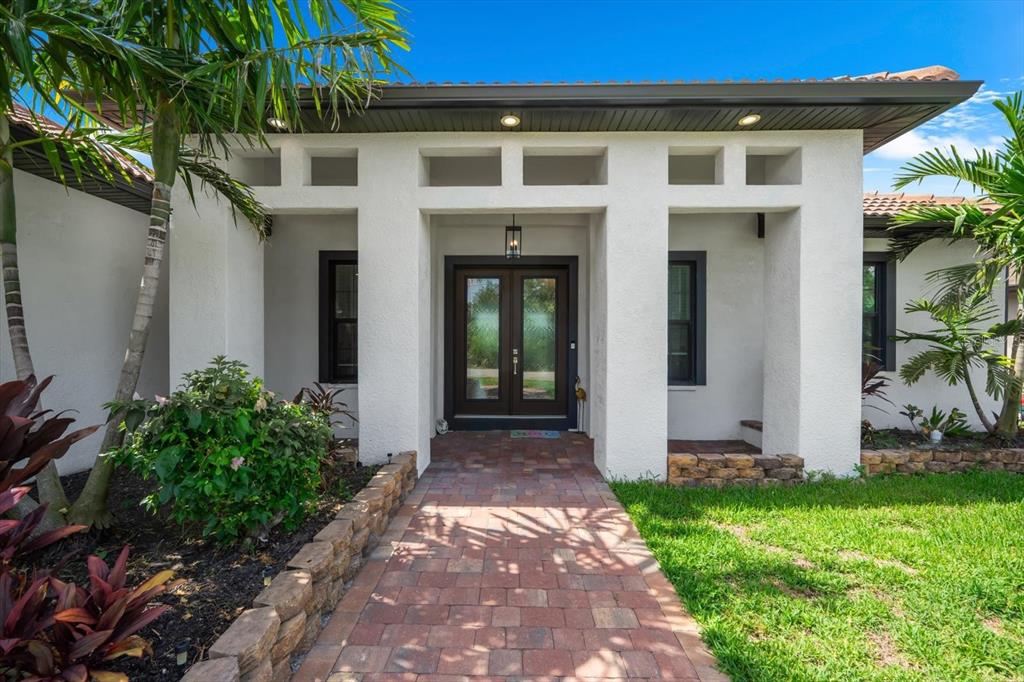 A paved walkway leads to the double front doors of a white stucco house — 15504 HENNIPEN CIRCLE, PORT CHARLOTTE, FL