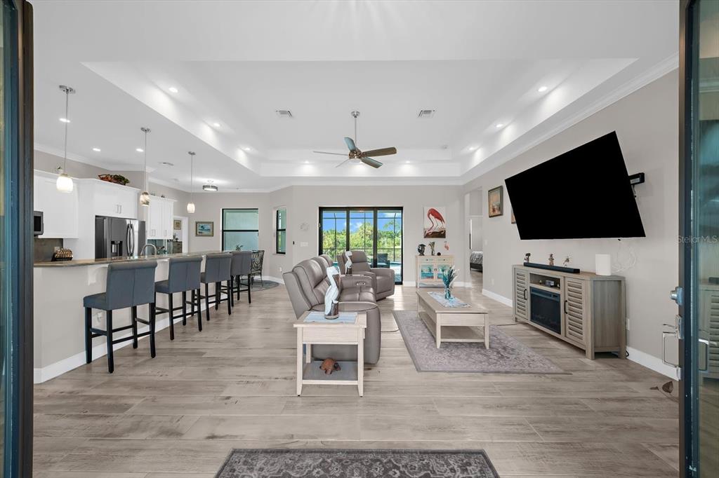 An open-concept living room and kitchen featuring light wood-look flooring and a tray ceiling — 15504 HENNIPEN CIRCLE, PORT CHARLOTTE, FL