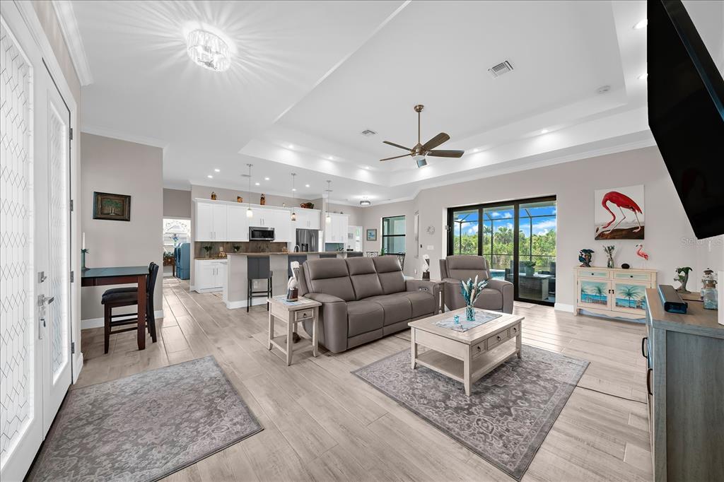 An open-concept living room features a tray ceiling, tile flooring, and a kitchen with white cabinetry — 15504 HENNIPEN CIRCLE, PORT CHARLOTTE, FL