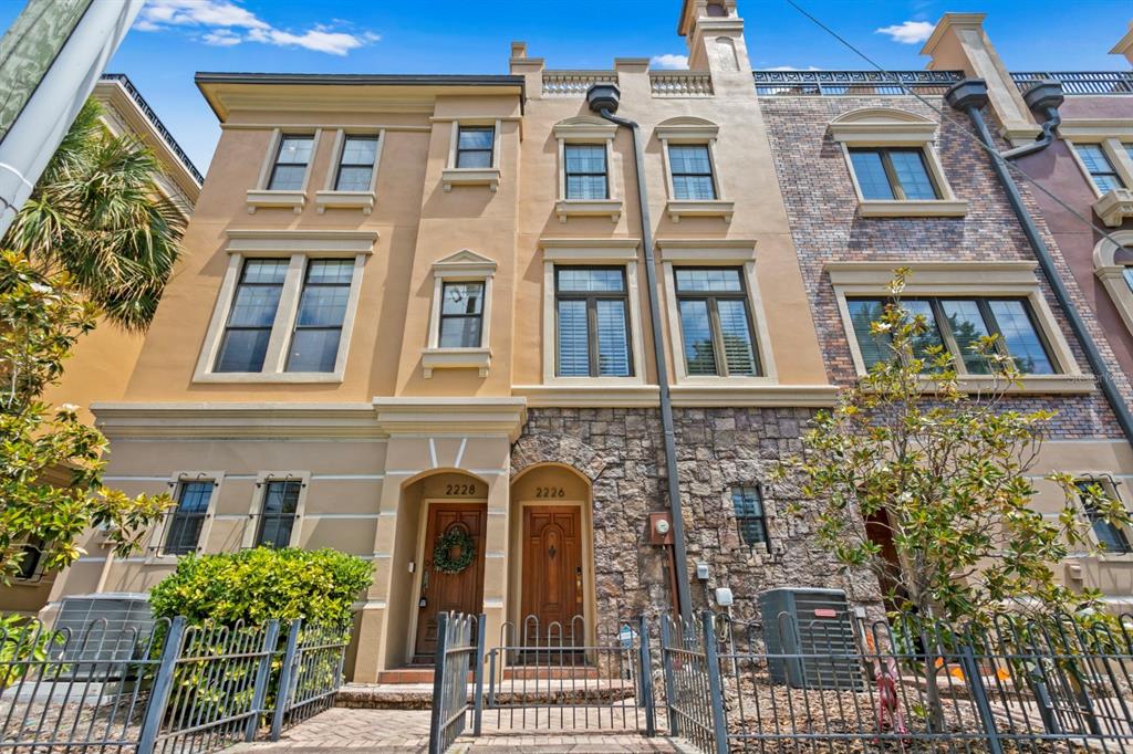 A low-angle exterior view of two adjacent multi-story townhouses with stone and stucco facades — 2226 SOHO BAY COURT, TAMPA, FL