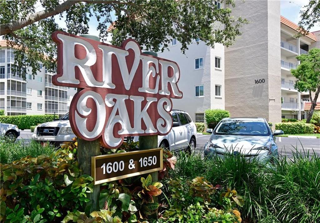 A sign for River Oaks stands in front of a multi-story apartment building — 1650 1ST AVENUE W UNIT 507B, BRADENTON, FL