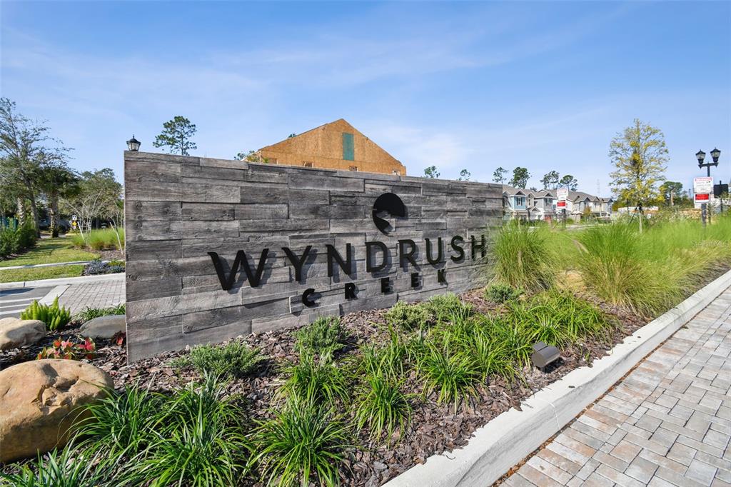 A wooden sign for Wyndrush Creek stands in a landscaped area near a paved road — 34214 CINDER WAY, WESLEY CHAPEL, FL