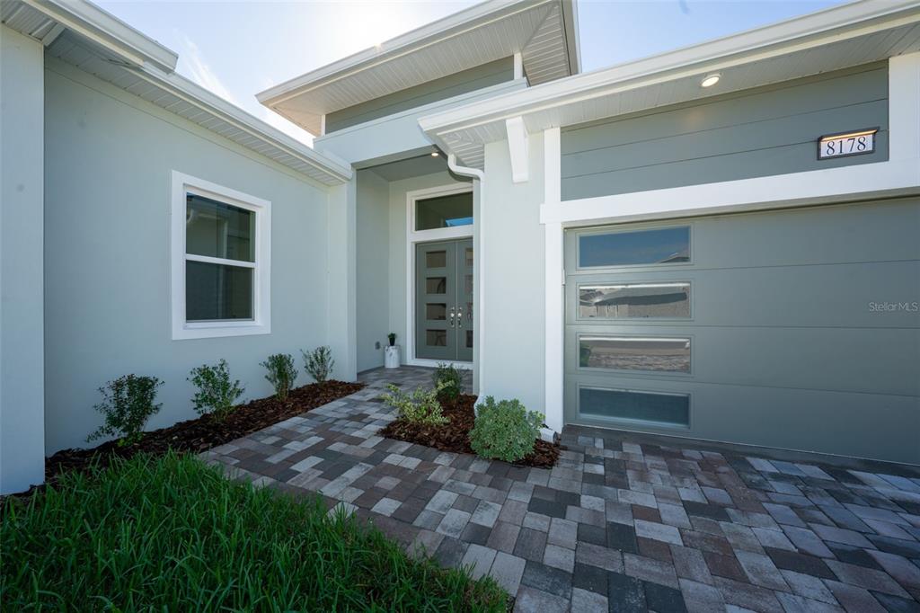 The exterior of a modern house features a paver driveway, a gray garage door, and a front entrance — 8178 IVY STARK BOULEVARD, WESLEY CHAPEL, FL