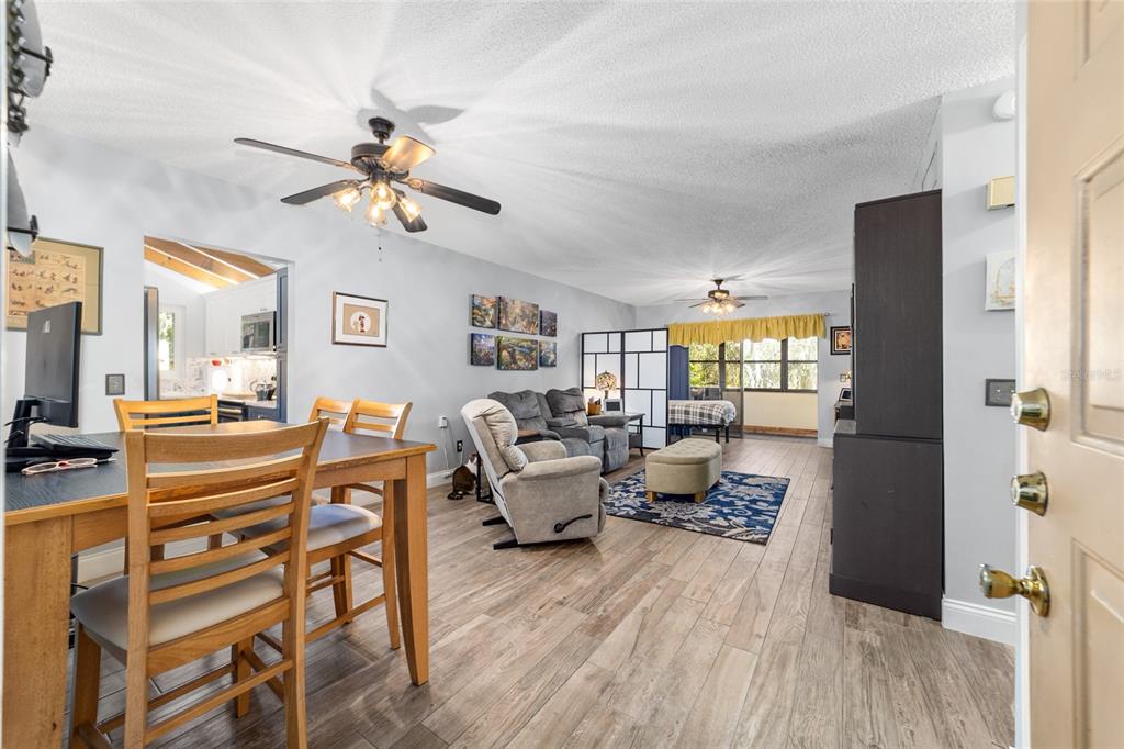 An open-concept living and dining area features wood-look flooring, ceiling fans, and a kitchen view — 3535 NE FORT KING STREET UNIT 261, OCALA, FL