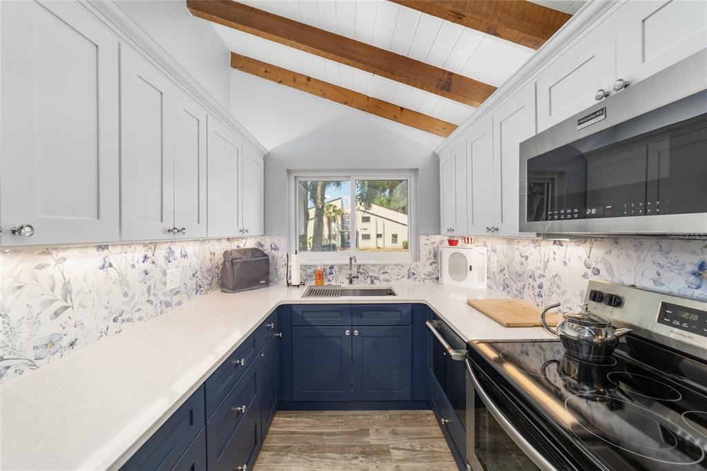 A galley kitchen features blue lower cabinets, white upper cabinets, floral backsplash, and wood ceiling beams — 3535 NE FORT KING STREET UNIT 261, OCALA, FL