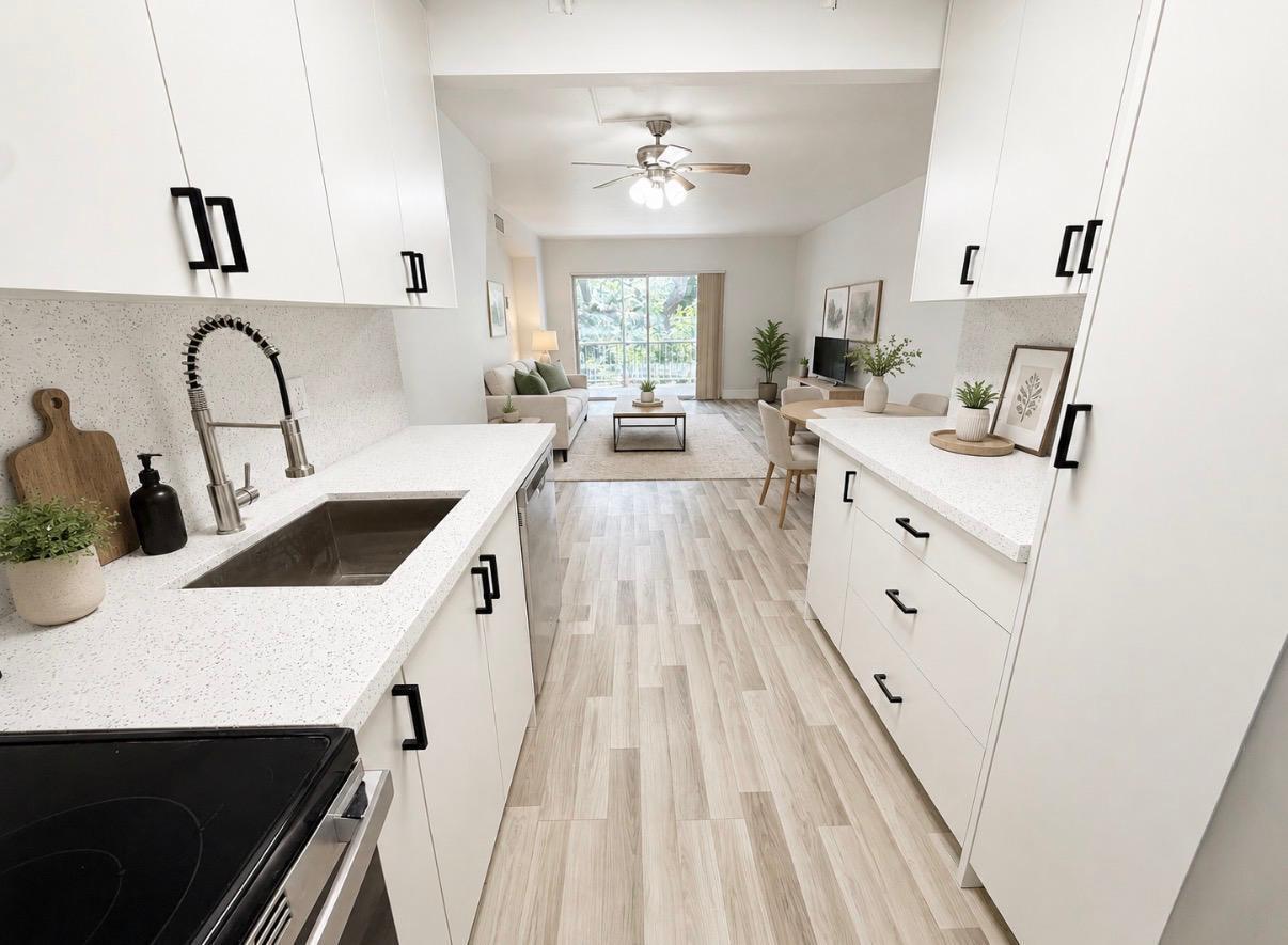A galley kitchen with white cabinets and speckled countertops opens into a living area — 610 NW 13th Street # 210, Boca Raton FL 33486, BOCA RATON, FL
