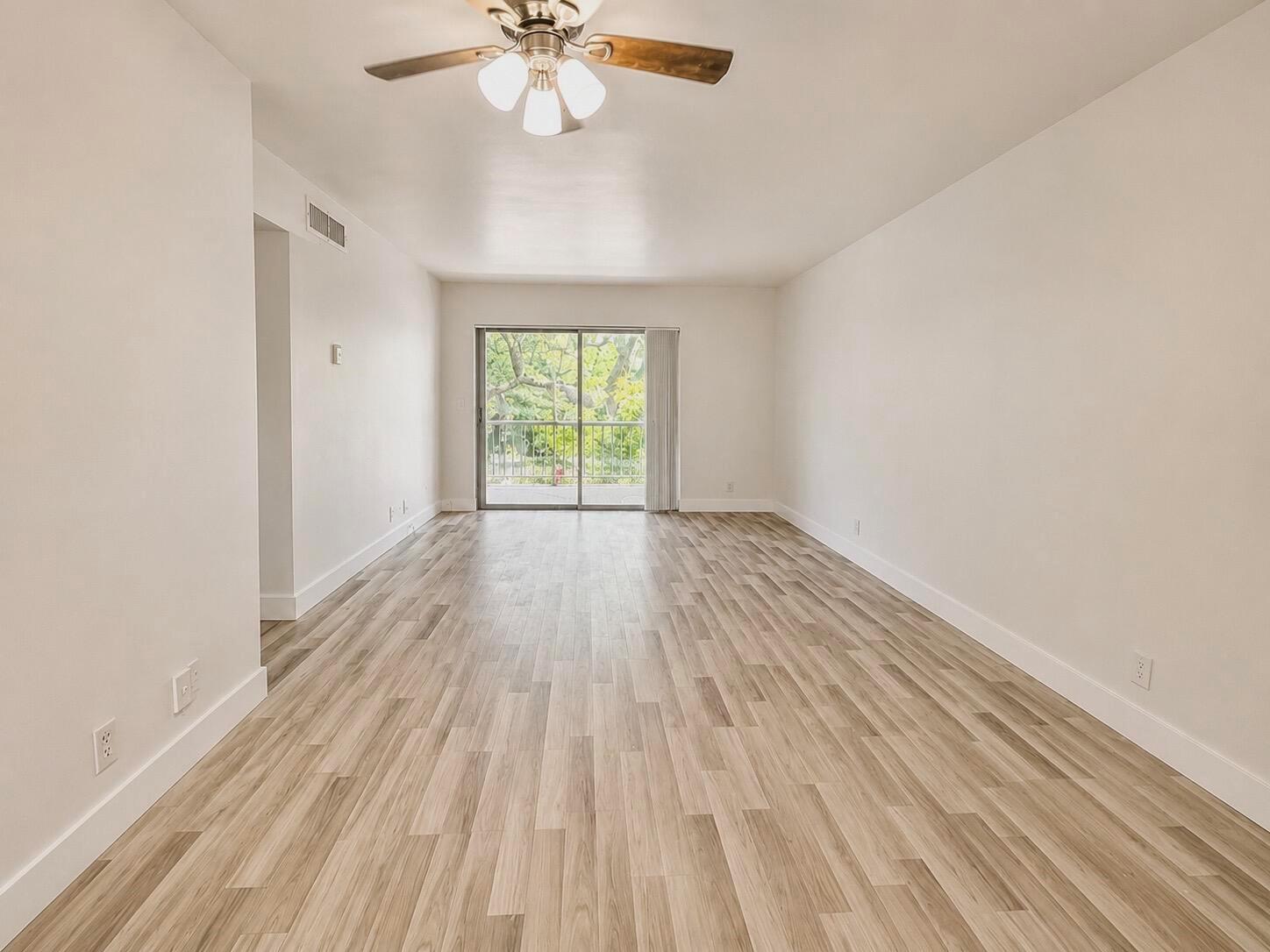 An empty living room features light wood-look flooring, white walls, and a sliding glass door — 610 NW 13th Street # 210, Boca Raton FL 33486, BOCA RATON, FL