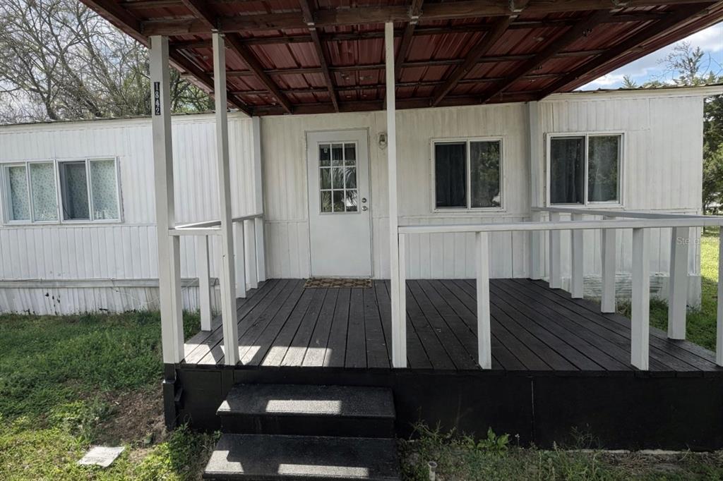 A mobile home exterior features a dark wooden deck, white siding, and a covered porch — 1842 NW 110TH COURT, OCALA, FL