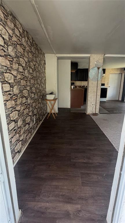A room with dark wood-look flooring and a stone-patterned accent wall leads to a kitchen — 1842 NW 110TH COURT, OCALA, FL