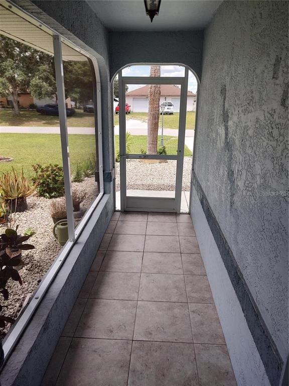 A tiled, screened-in entryway features a light fixture and a view of the front yard — 2051 LOGSDON STREET, NORTH PORT, FL