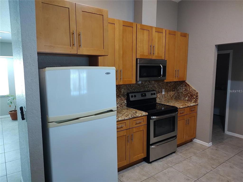A kitchen features light wood cabinets, granite countertops, and stainless steel appliances — 2051 LOGSDON STREET, NORTH PORT, FL