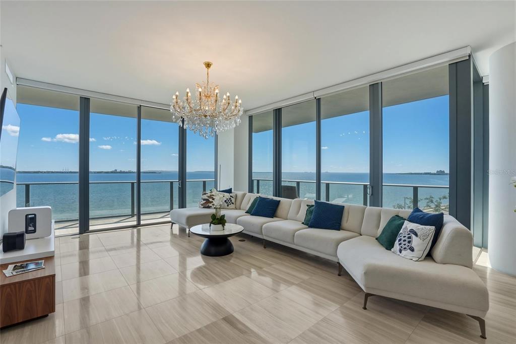 A modern living room features a large sectional sofa, crystal chandelier, and floor-to-ceiling ocean views — 3101 BAYSHORE BOULEVARD UNIT 504, TAMPA, FL