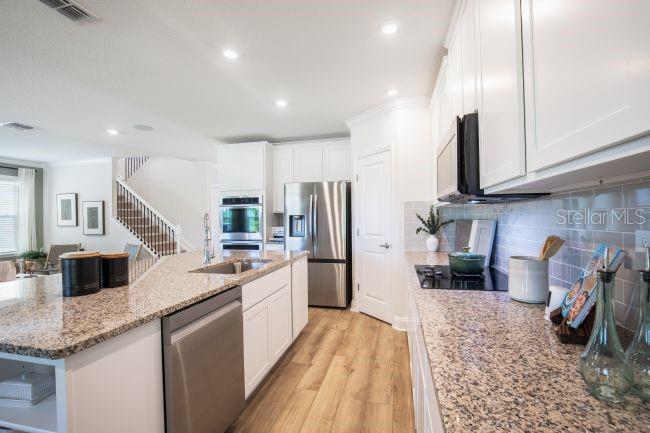 A kitchen features white cabinetry, granite countertops, stainless steel appliances, and light wood-look flooring — 30621 PRESTWICK AVENUE, SORRENTO, FL