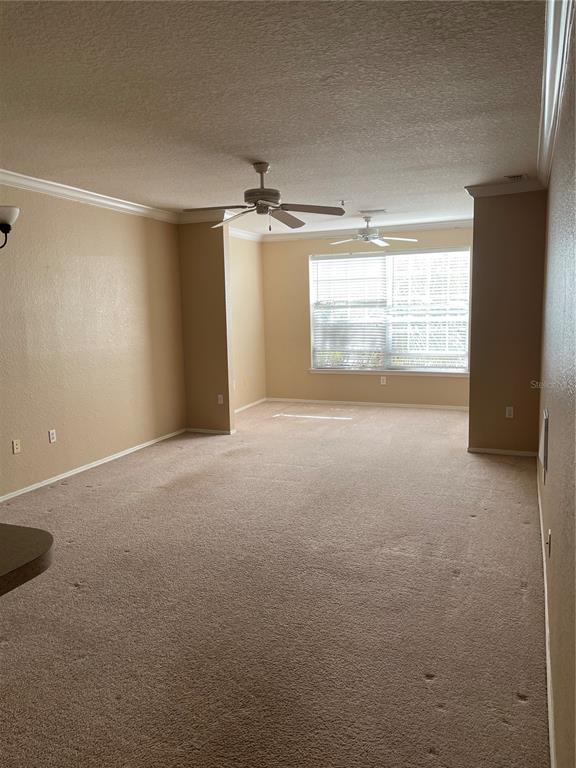 An empty living room features beige carpet, tan walls, crown molding, and two ceiling fans — 3355 S KIRKMAN ROAD UNIT 1324, ORLANDO, FL