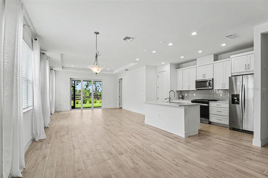 A bright, open-concept kitchen and living area features white cabinetry, stainless appliances, and wood-look flooring — 44283 PANTHER DRIVE, PUNTA GORDA, FL