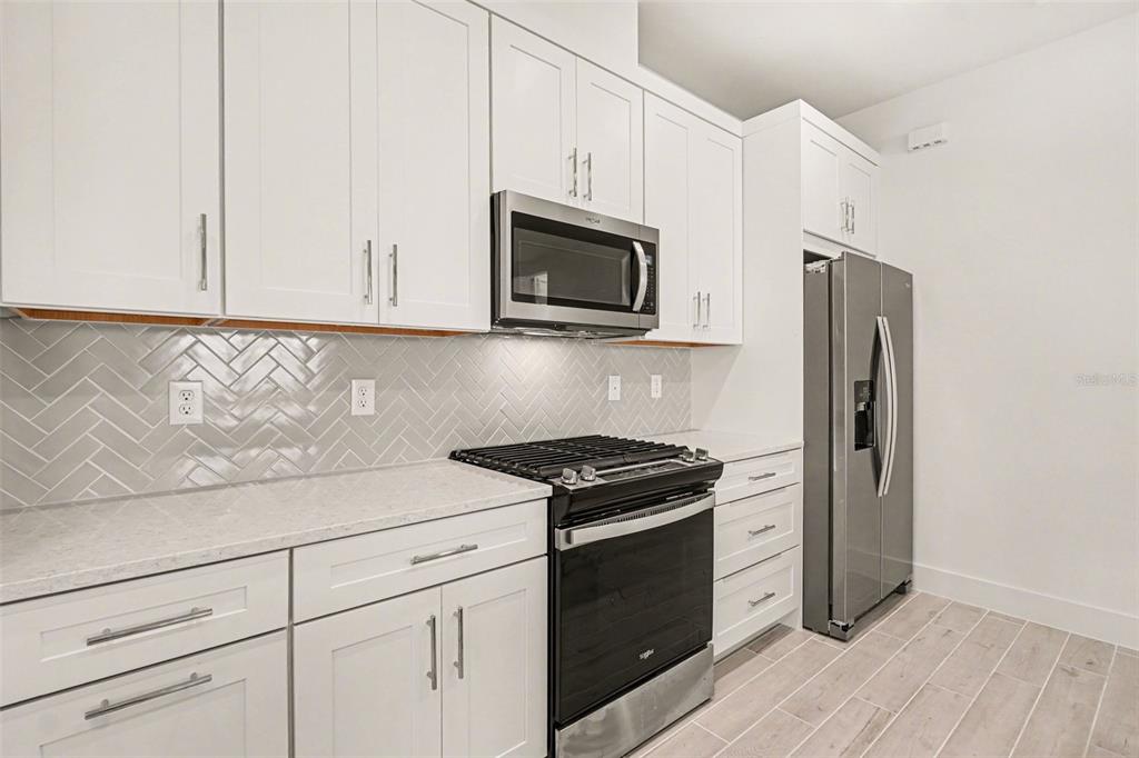 A kitchen features white cabinets, stainless steel appliances, and a gray herringbone tile backsplash — 44283 PANTHER DRIVE, PUNTA GORDA, FL