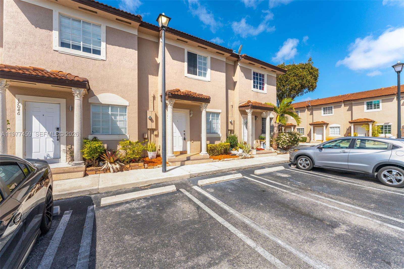 A row of two-story townhouses with beige stucco exteriors and tiled roofs faces a parking lot — 17040 SW 137th Pl, Miami FL 33177, MIAMI, FL
